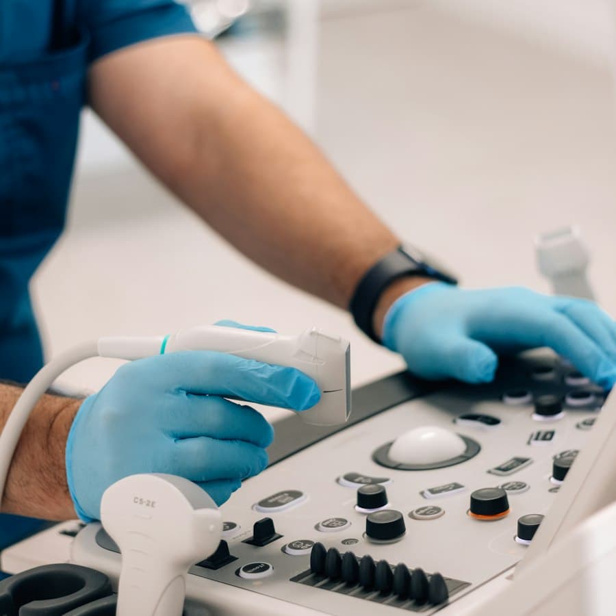 Mãos com luvas operando aparelho de ultrassom